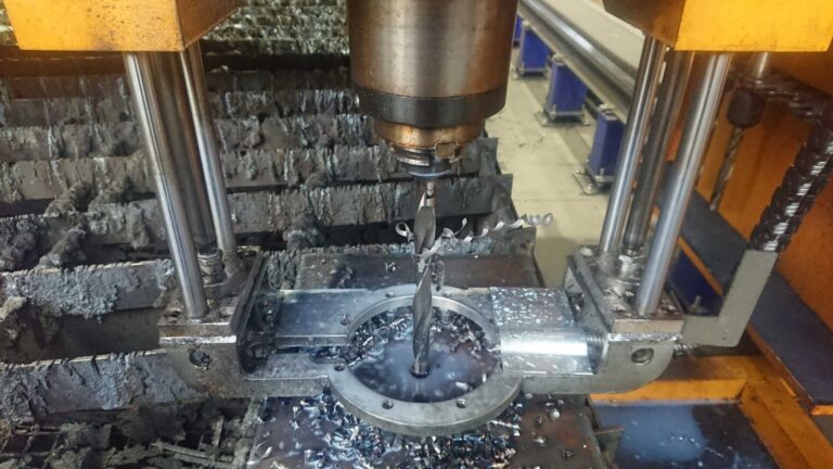 Drilling tool station drilling into material held on the cutting table by a retainer